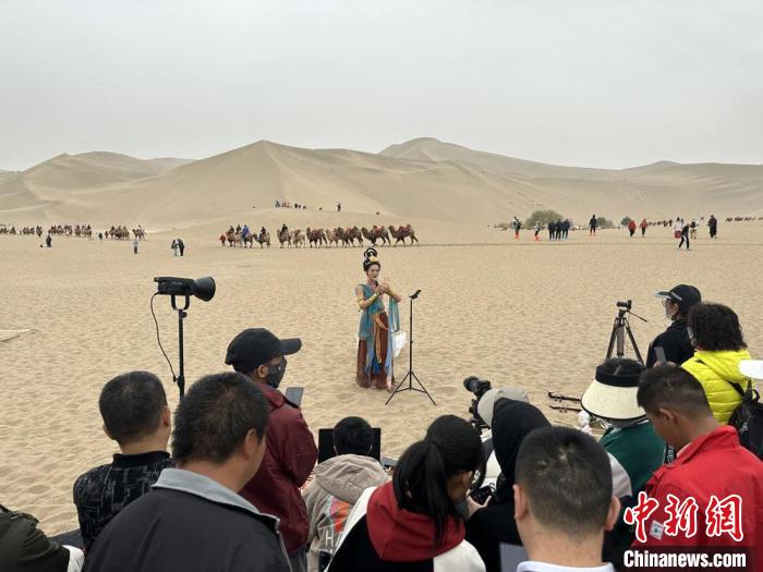 圖為2023年4月底，敦煌大漠“逐舞者”奧楠在鳴沙山月牙泉景區(qū)視頻直播，吸引游人圍觀?！●T志軍 攝